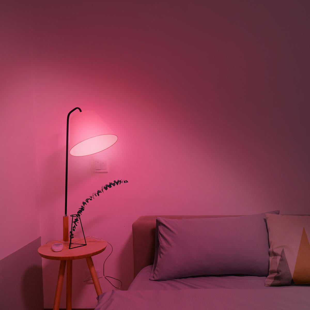 Eine moderne Stehlampe mit rundem Schirm beleuchtet ein Schlafzimmer mit rosa Wänden und Bett.