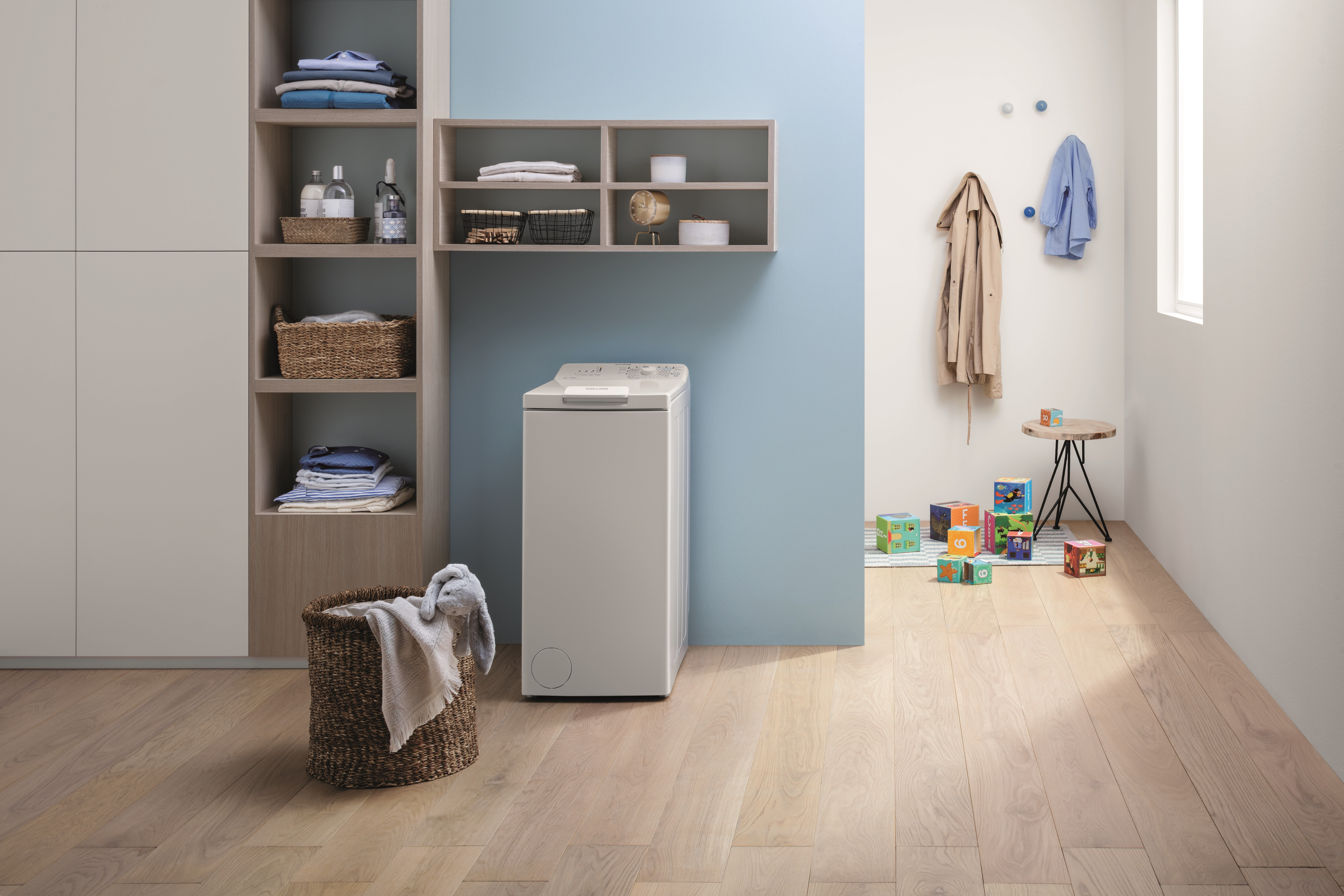 Waschküche: Waschmaschine, Wäschekorb, Regale, Holzfußboden, blaue Wand.