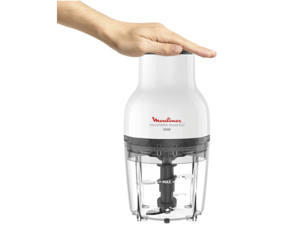 Picadora de alimentos Moulinex blanca, recipiente transparente, cuchillas negras, una mano encima.