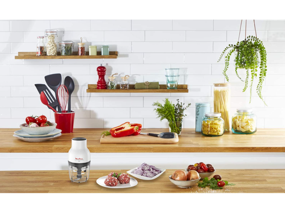 Escena de cocina con comida, utensilios y un pequeño procesador de alimentos.