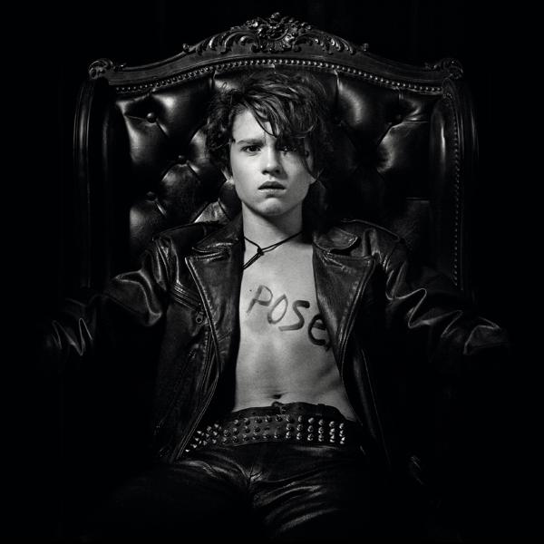 A black and white photo of a young man in a leather jacket, with 'POSE' written on his chest.