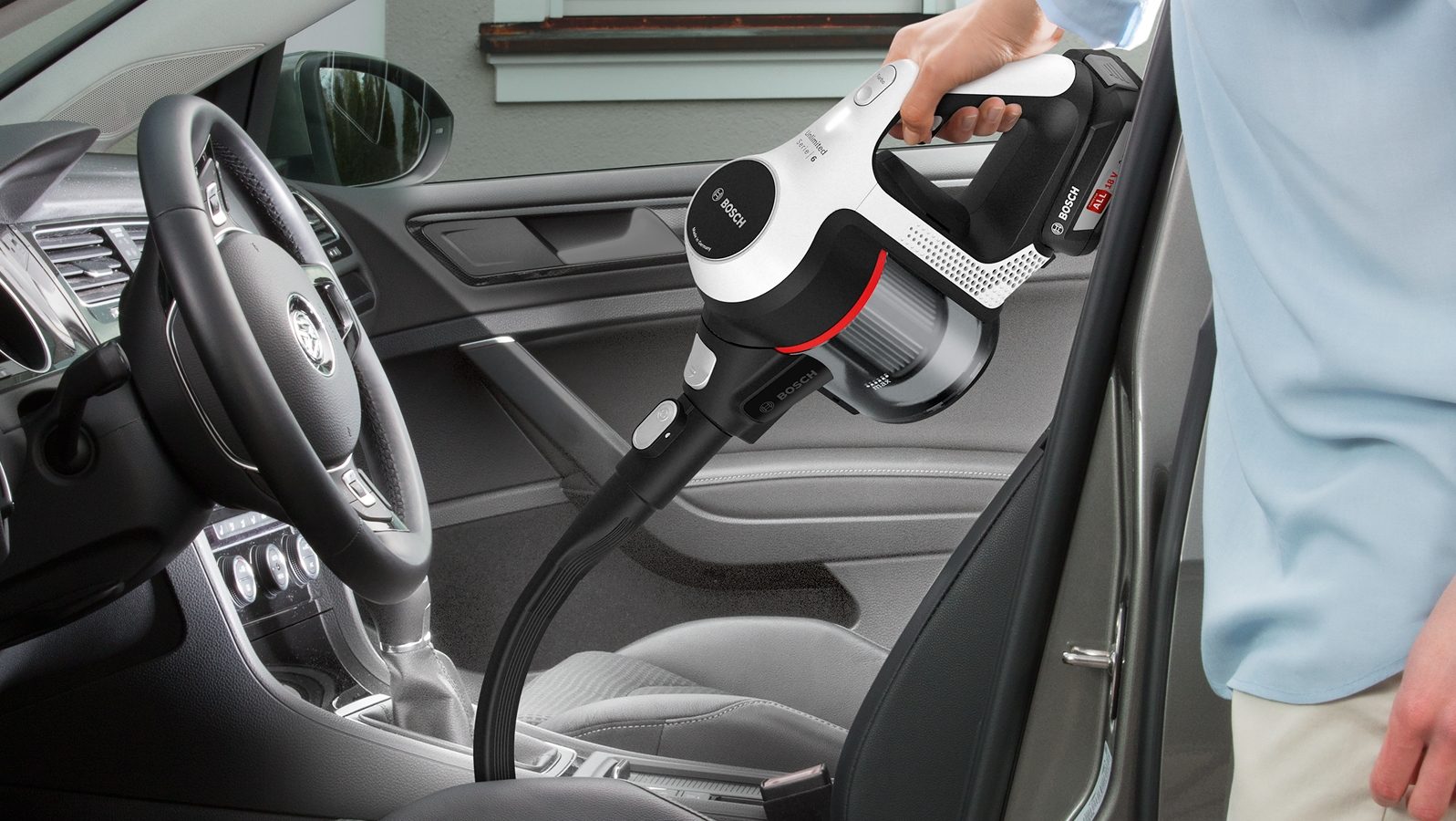 Eine Person, die einen Autoinnenraum mit einem Handstaubsauger absaugt.