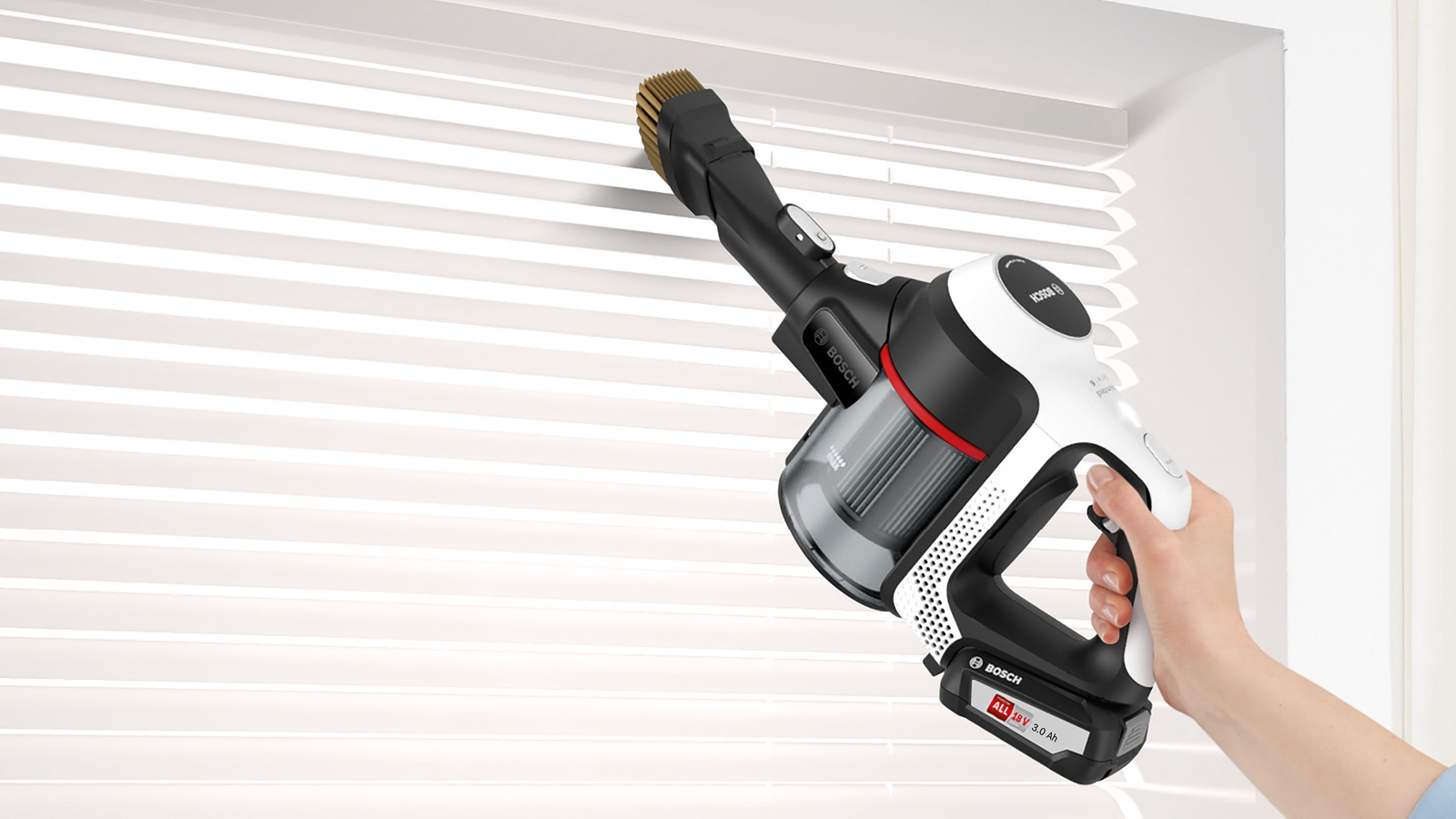 Eine Hand benutzt einen Bosch-Staubsauger, um weiße Jalousien zu reinigen. Der Hintergrund ist hell.