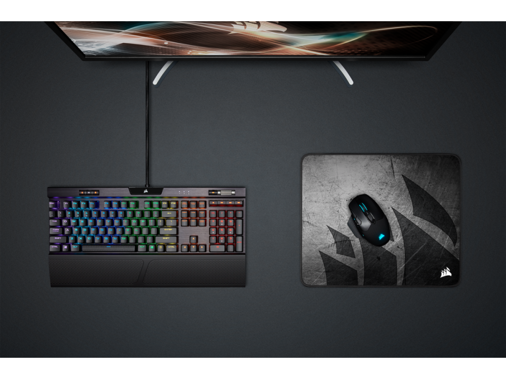 Un teclado, un ratón y una alfombrilla de ratón están sobre una superficie oscura. El teclado tiene iluminación RGB.