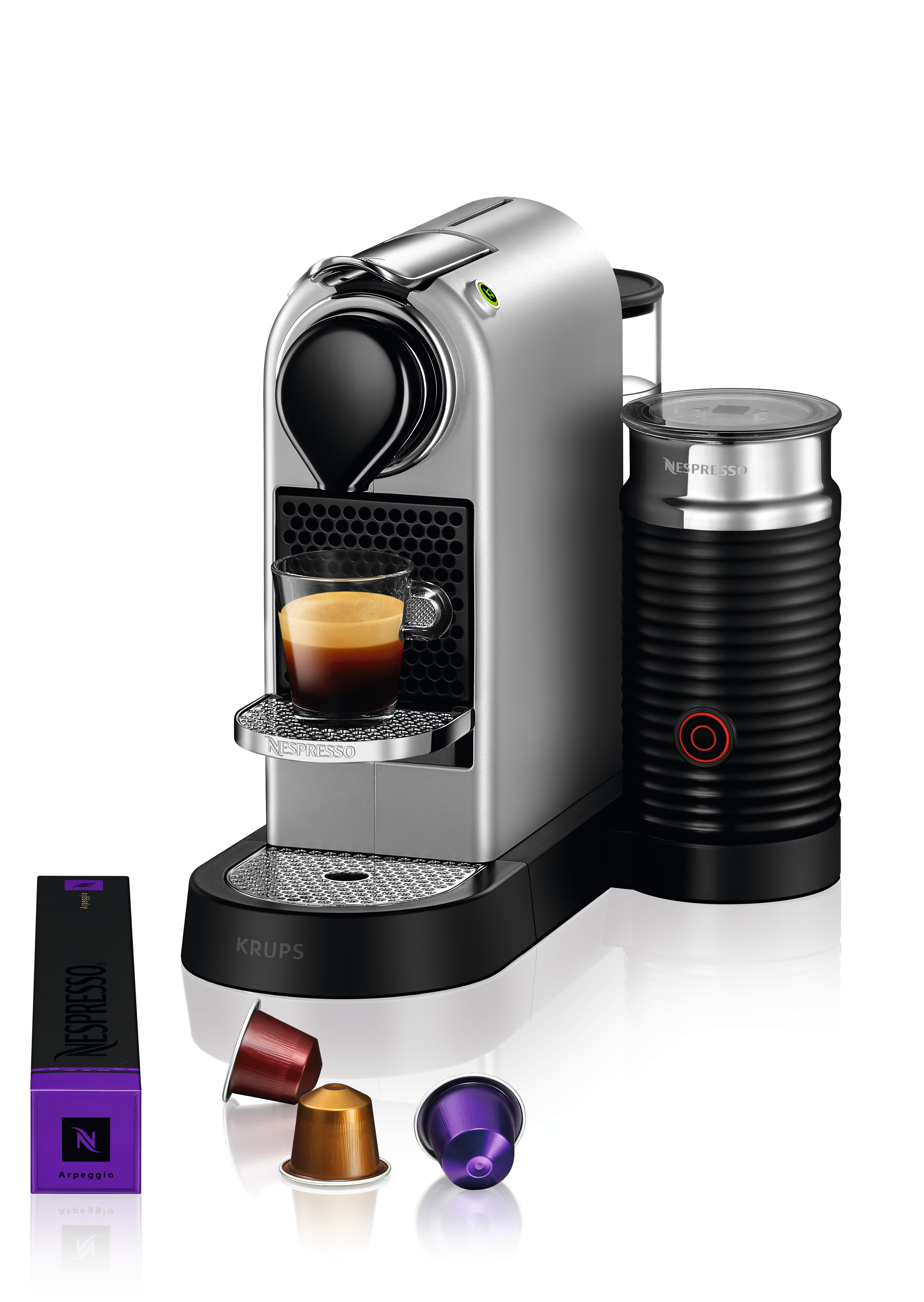 Eine silberne Krups Nespresso Maschine, Kaffee wird in ein Glas ausgeschenkt, mit Kapseln.