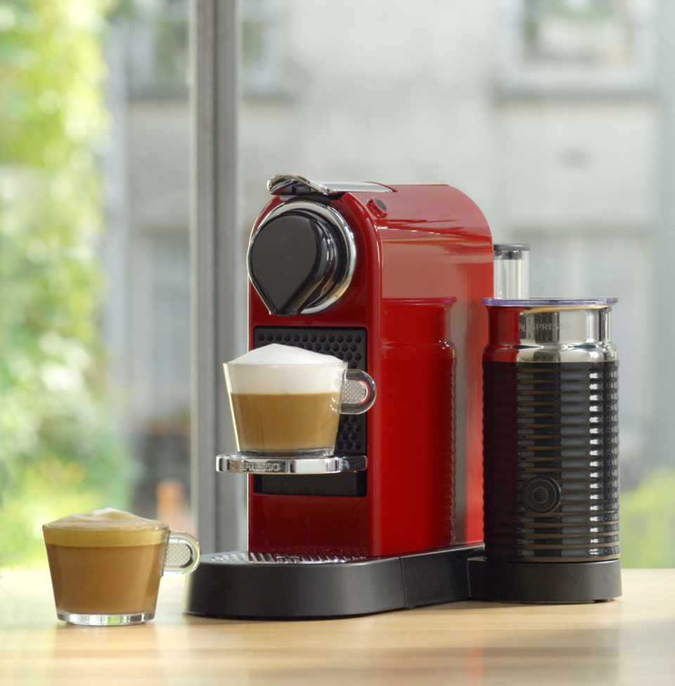Eine rote Nespresso-Maschine mit einer Tasse Kaffee und Milchaufschäumer.