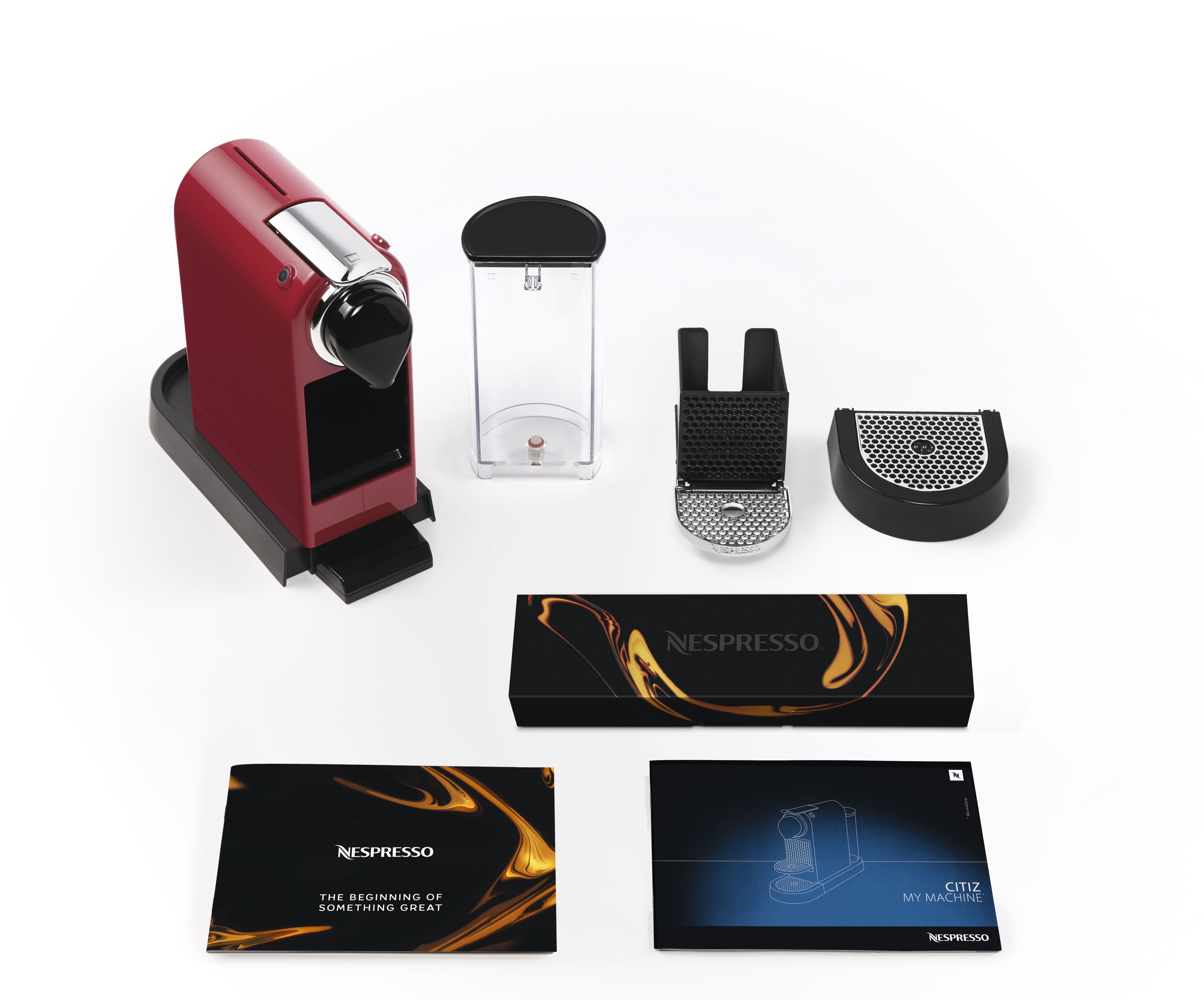Eine rote Nespresso-Maschine mit Zubehör und Bedienungsanleitungen auf weißem Hintergrund.