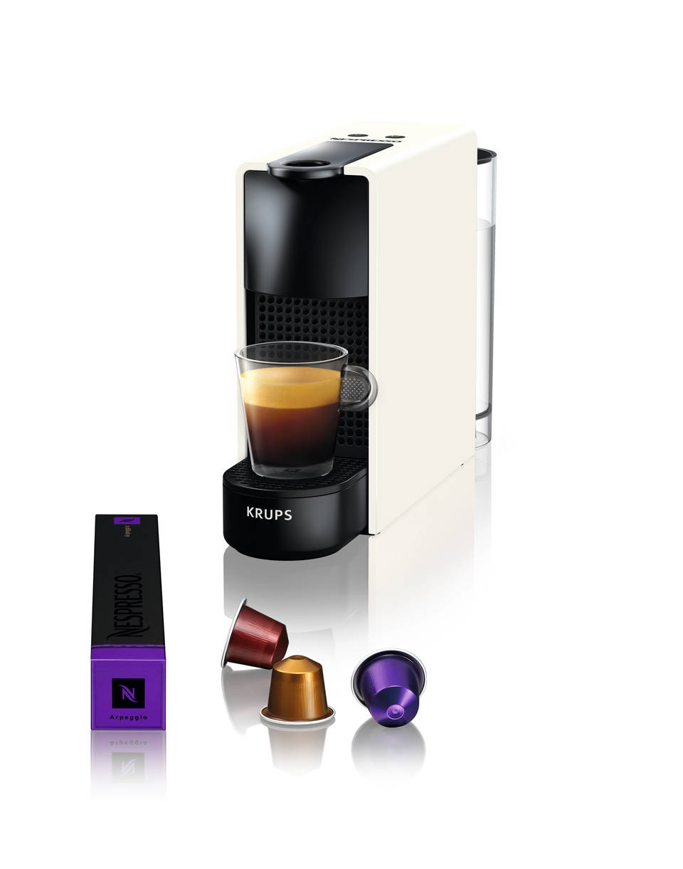 Weiße Krups Nespresso Maschine mit einem Glas Kaffee und Kaffeekapseln.