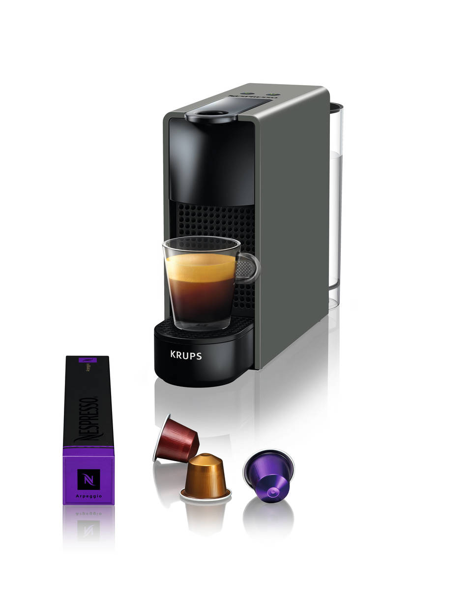 Eine graue Nespresso-Kaffeemaschine mit Kaffeekapseln und einem Glas Kaffee.
