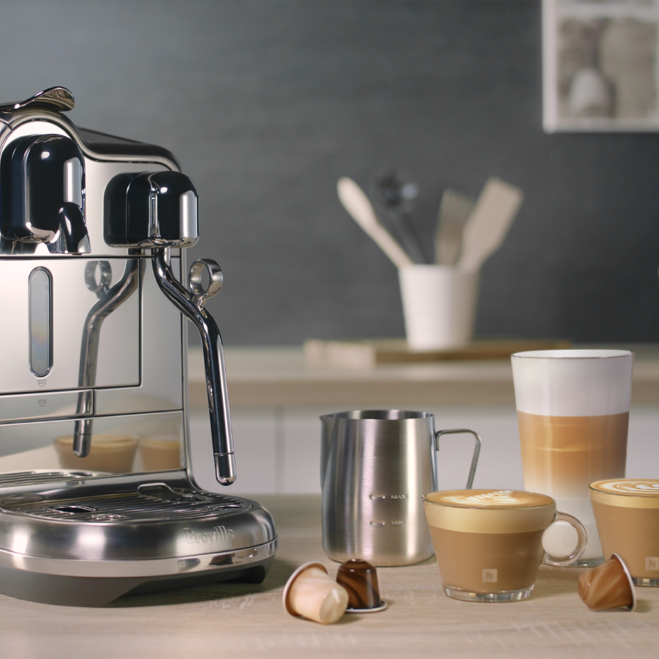 Espressomaschine mit Kaffeetassen und einem Milchaufschäumer. Kaffeebohnen sind auf dem Tisch verstreut.