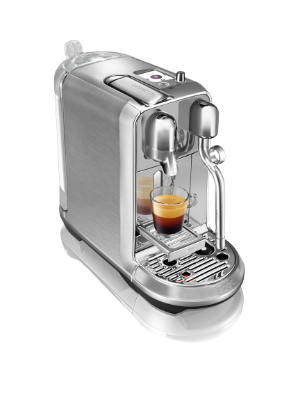 Silberne Nespresso-Kaffeemaschine mit einer Tasse Espresso. Weiße Basis, schwarzer Hintergrund.