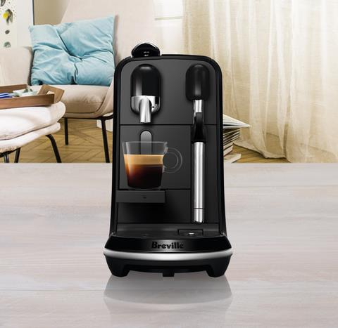 Schwarze Kaffeemaschine mit Tasse auf Tisch, in einem Raum.