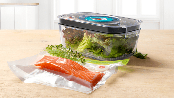Ein Vakuum-Lebensmittelbehälter mit Salat und Lachs. Andere Zutaten sind in der Nähe.