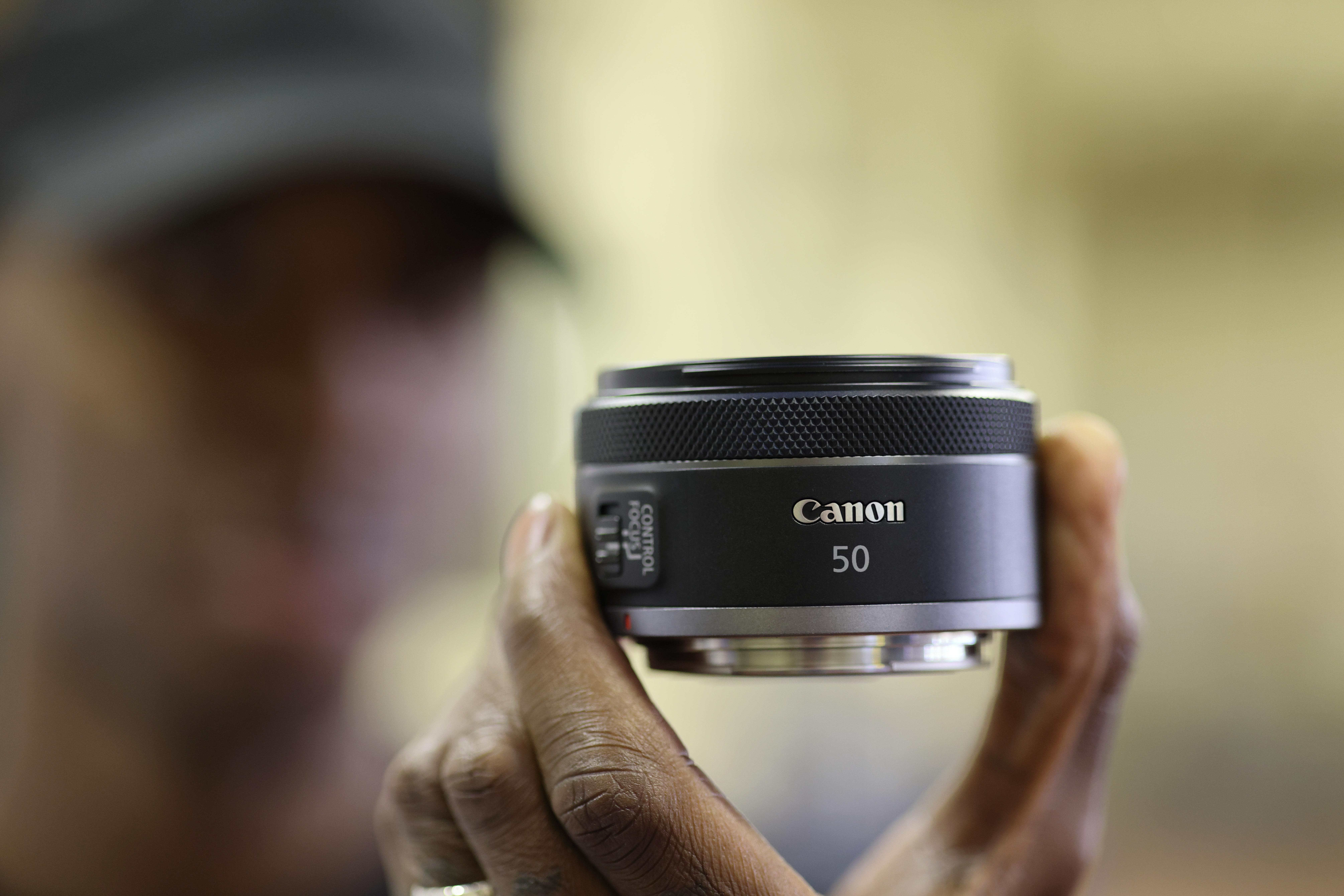 Ein Mann hält ein Canon 50mm Objektiv. Das Etikett zeigt die Marke und die Brennweite.