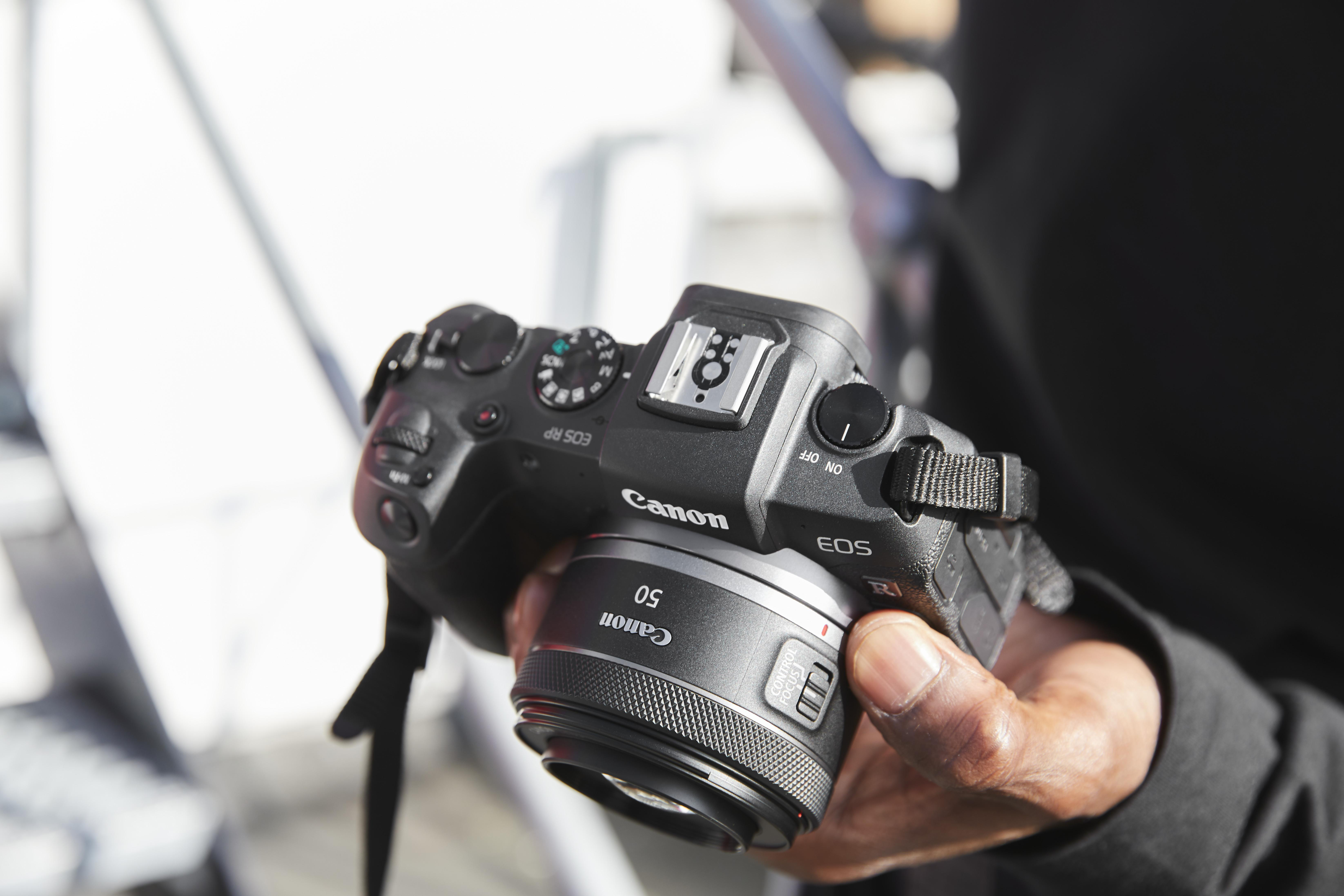 Eine Hand hält eine schwarze Canon-Kamera mit Objektiv, das Canon-Logo ist sichtbar.