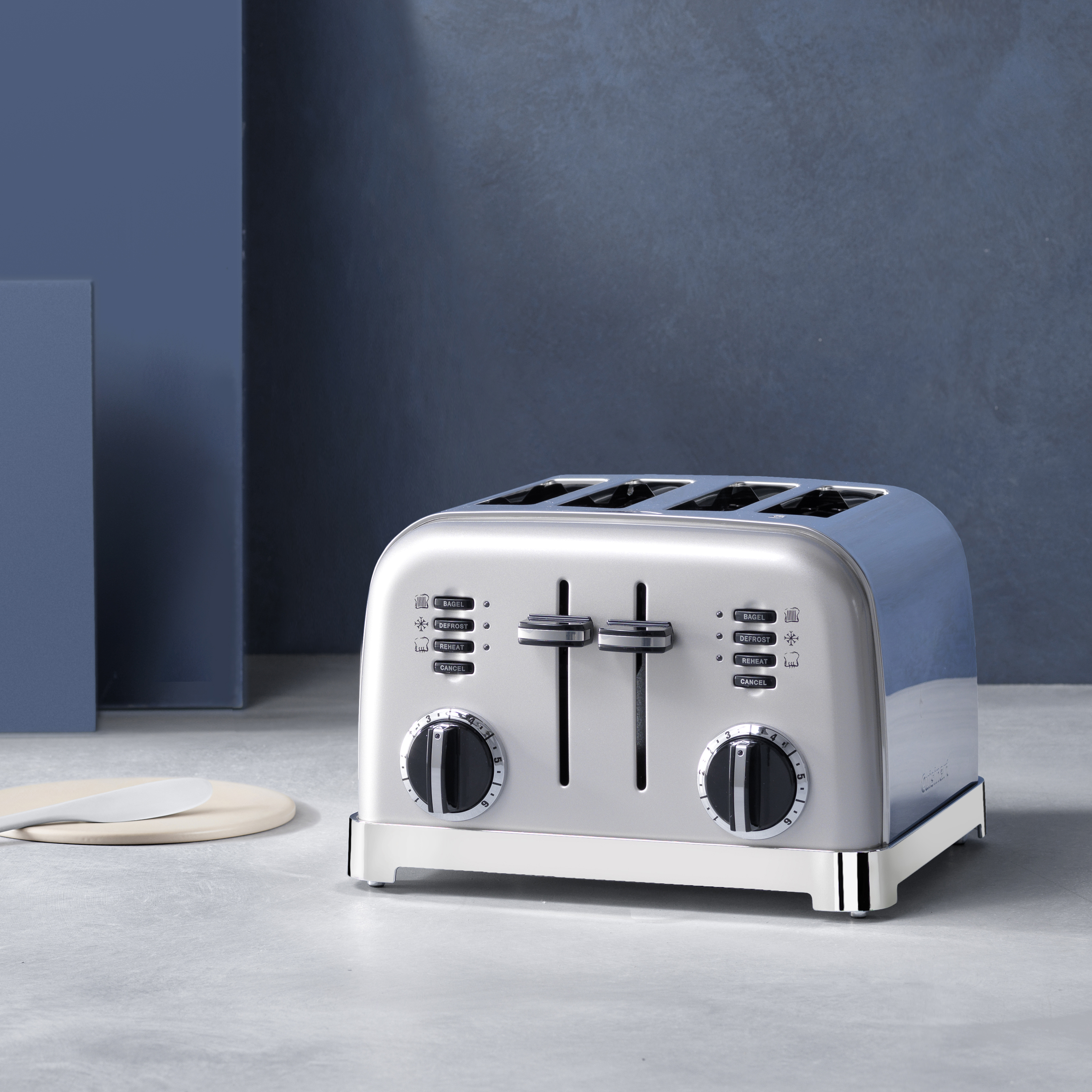 Silver and blue toaster with controls. White counter and blue background.
