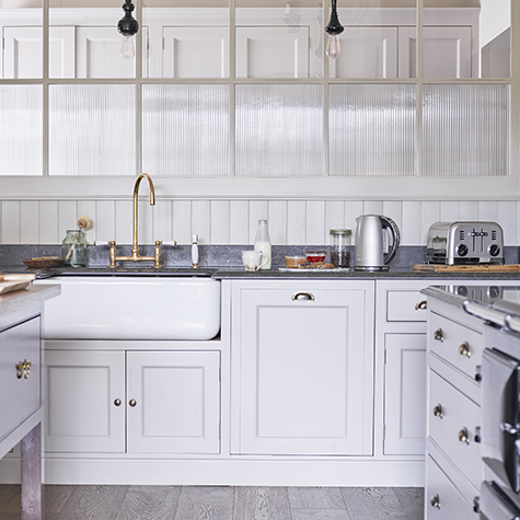 Kitchen interior with white cabinets, sink, and appliances. Grey countertop, light wood flooring.