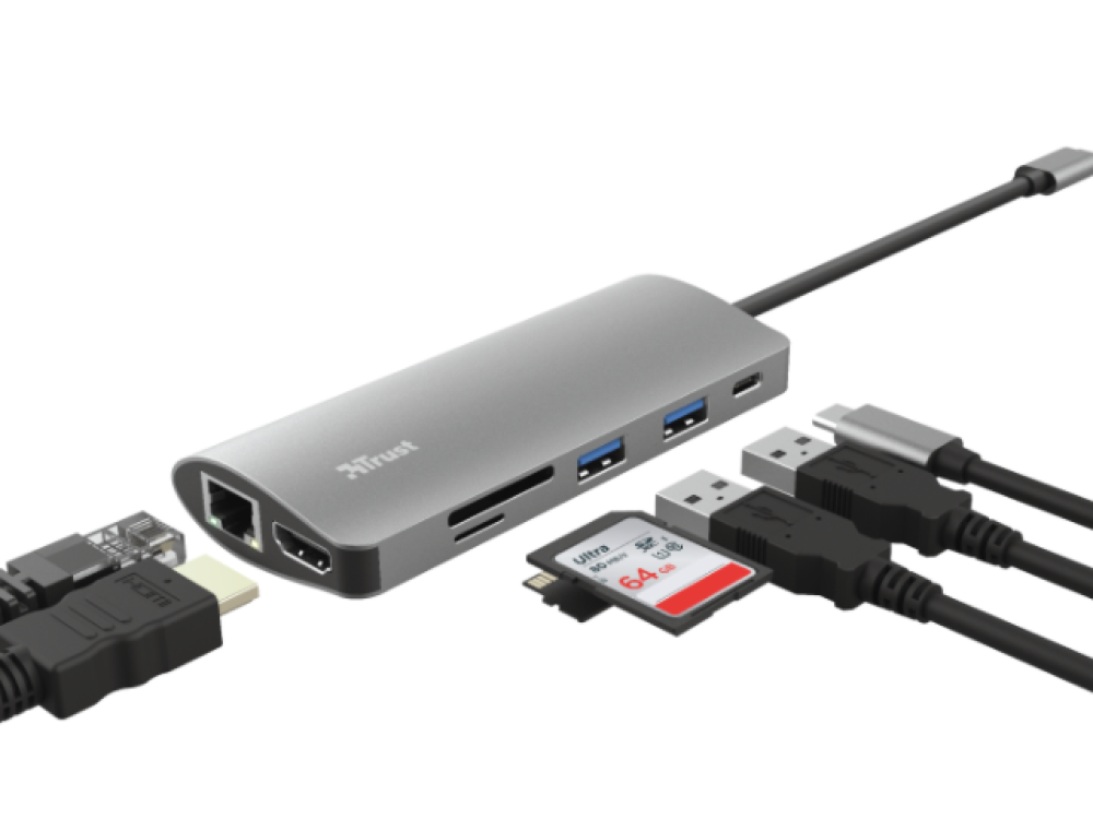 Concentrador USB-C plateado Trust con varios puertos y cables conectados. Fondo blanco.