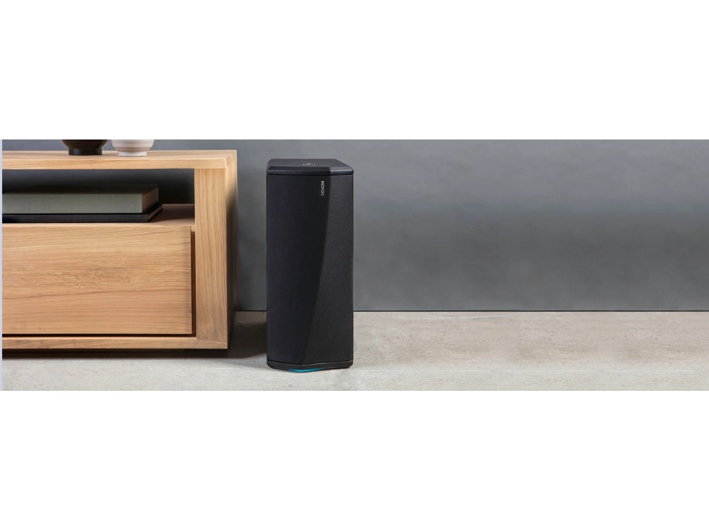Altavoz negro junto a un armario de madera. El fondo es una pared y suelo gris.