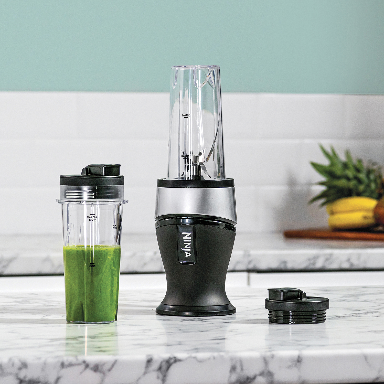 Blender with two cups. One filled with green liquid. White background.