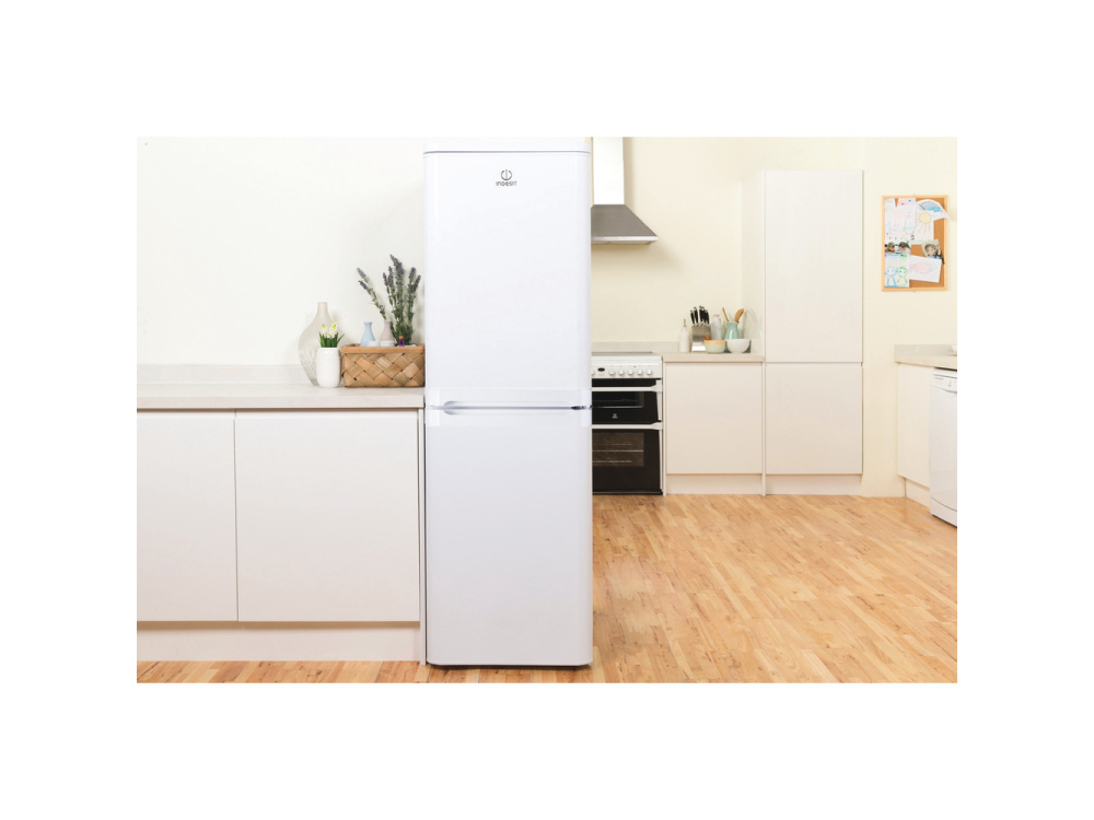 Una nevera blanca de dos puertas en una cocina. Suelo de madera, armarios y encimeras blancas.