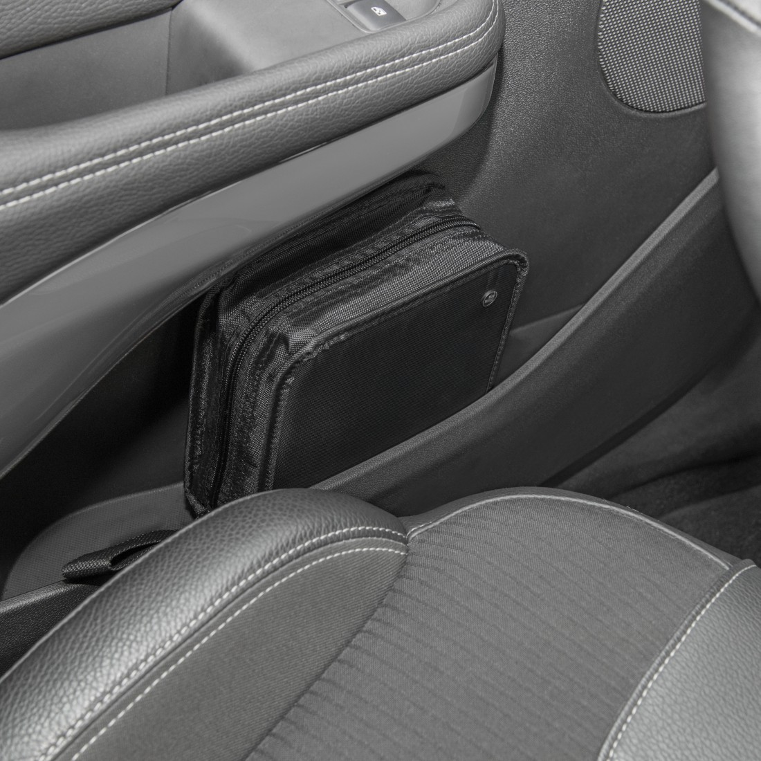 Schwarze Tasche in der Tasche des Autos. Der Innenraum des Autos ist grau. Die Tasche ist zugezippt.