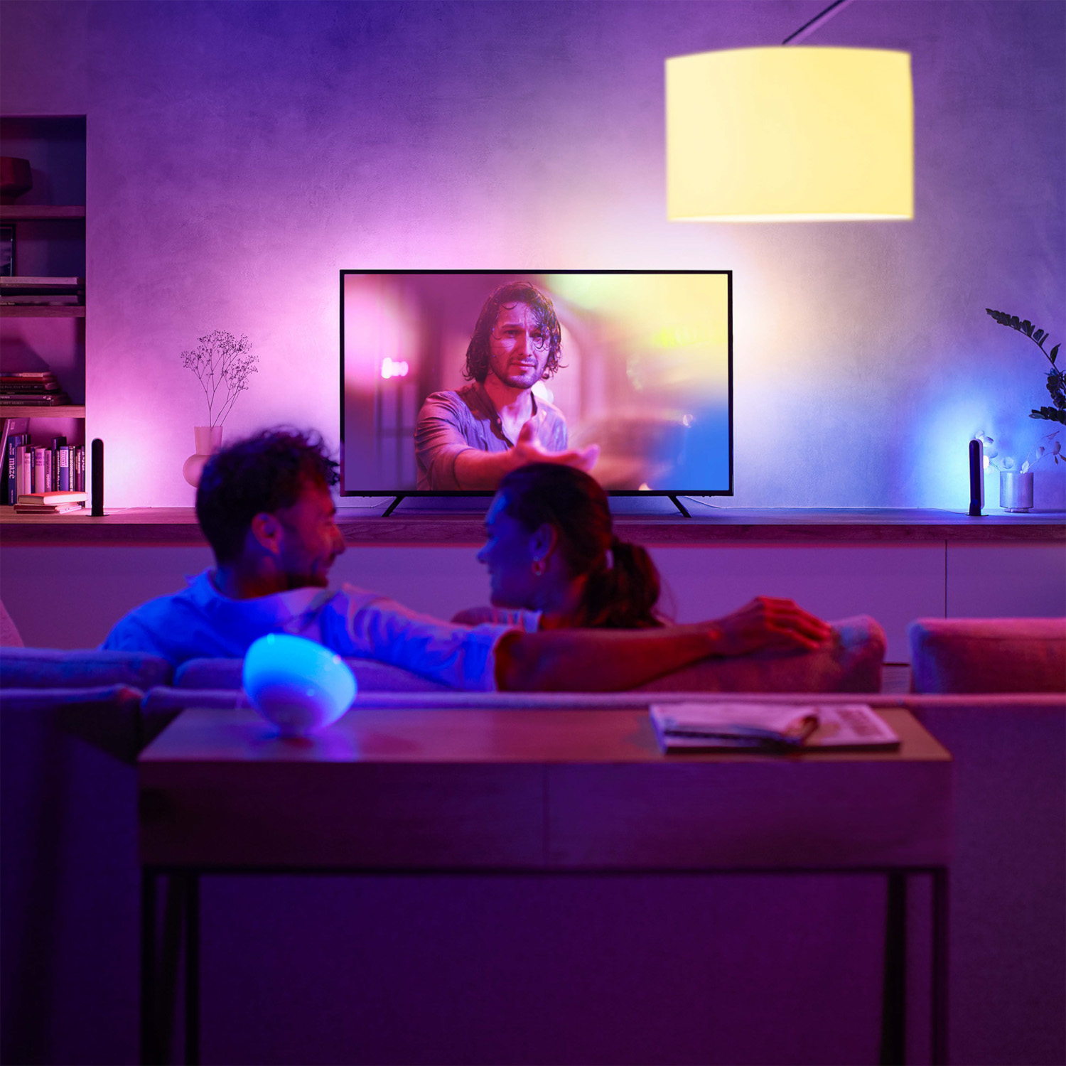 Couple in a living room with a TV. Ambient lighting, including colored light bars.