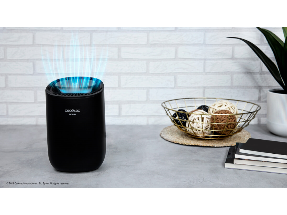 Un purificador de aire negro con luz azul que emite hacia arriba, con decoraciones sobre una mesa.