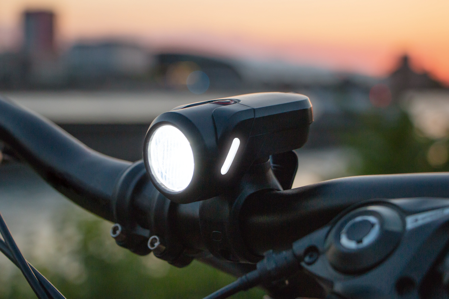 Fahrradscheinwerfer am Lenker, weißes Licht. Sonnenuntergang im Hintergrund.