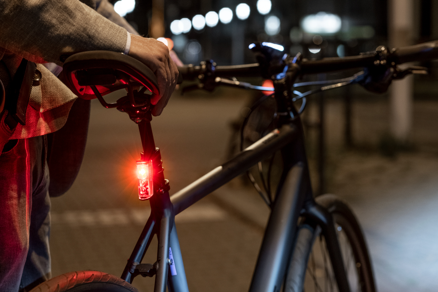 Eine Person mit einem Fahrrad in der Nacht, das Fahrrad hat ein rotes Rücklicht.