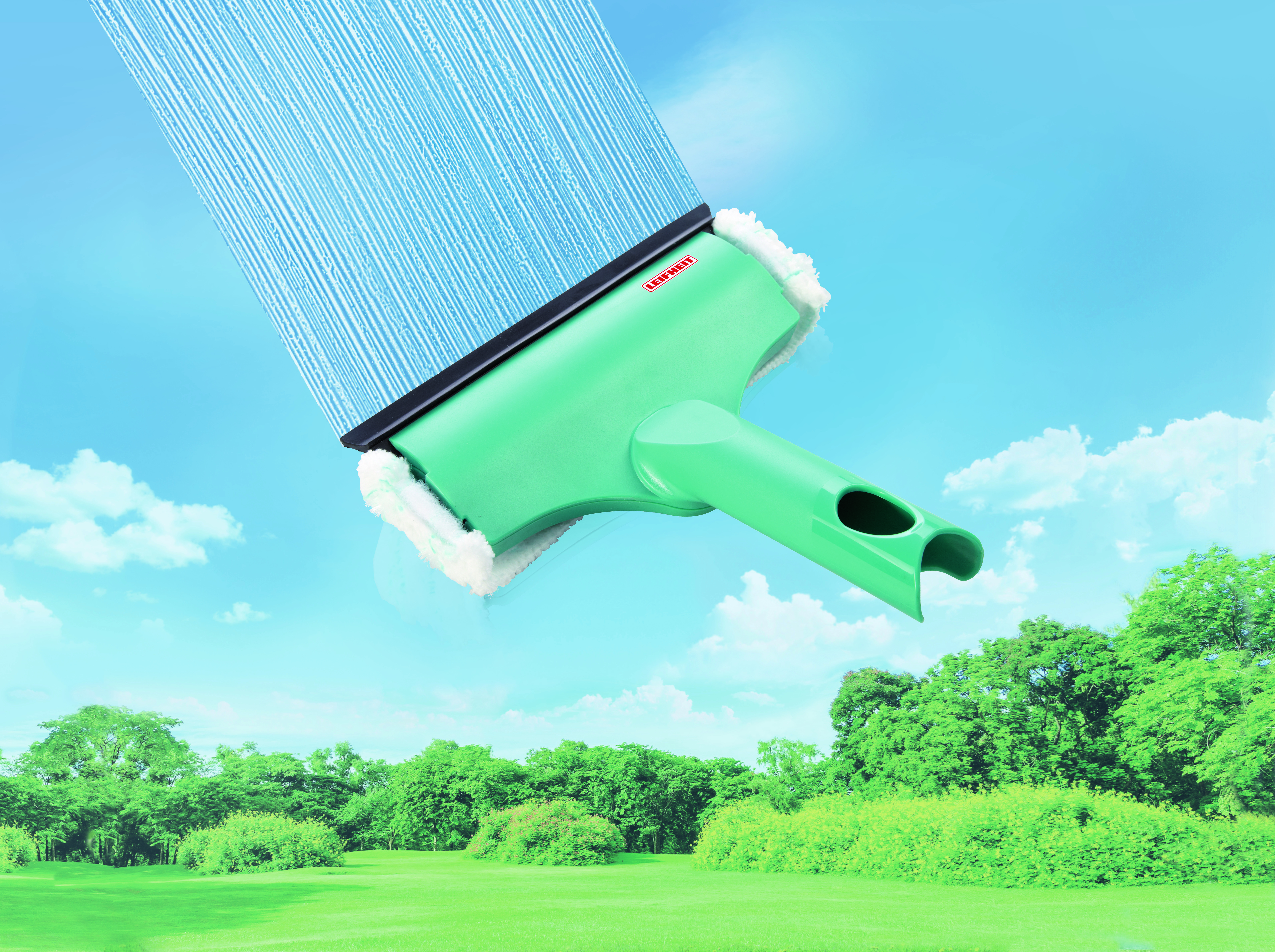 Ein grüner Fensterreiniger vor blauem Himmel mit Wolken und einer grünen Wiese mit Bäumen.