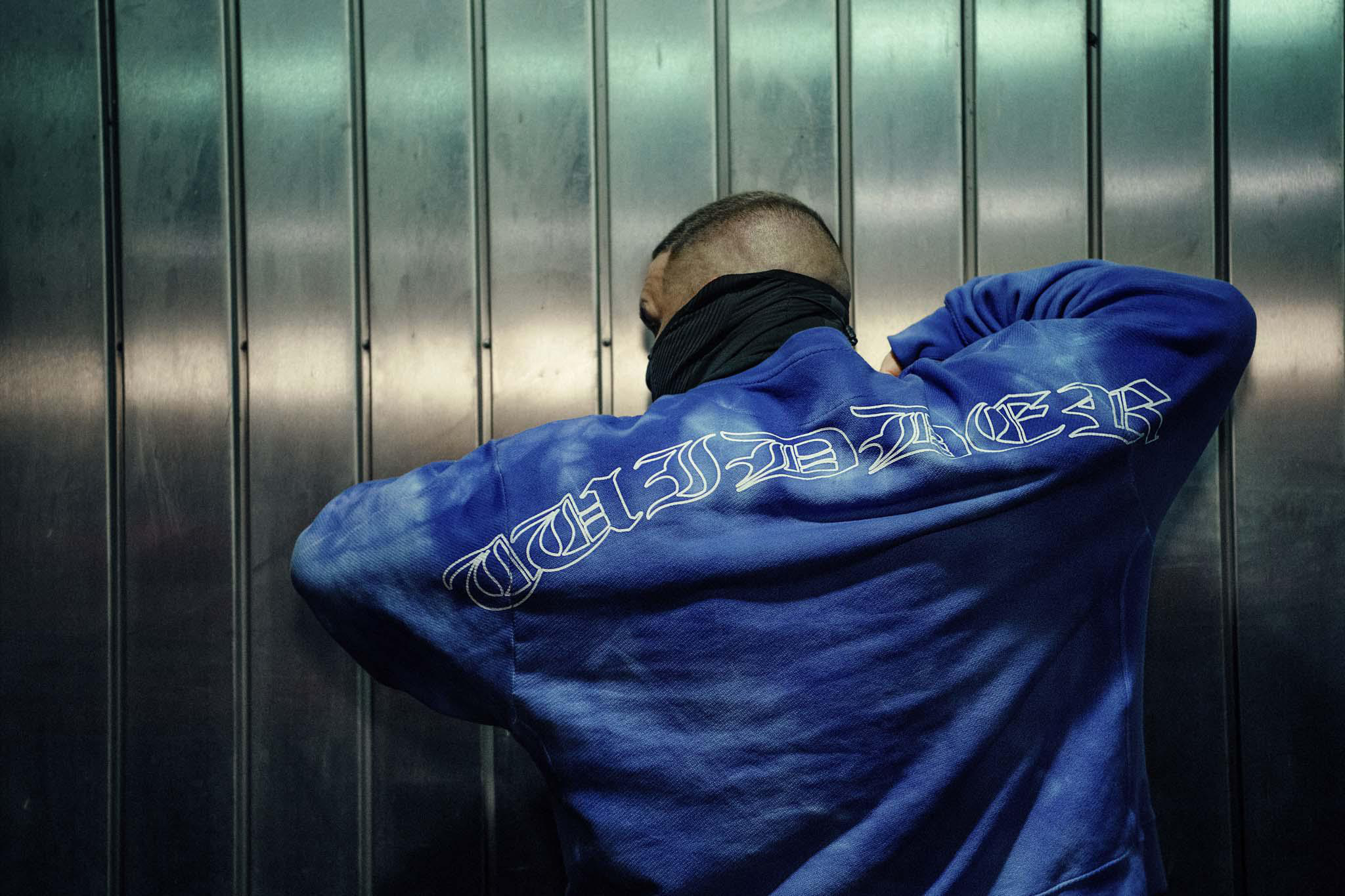 Eine Person in einem blauen Batik-Hoodie mit weißem Text auf dem Rücken.