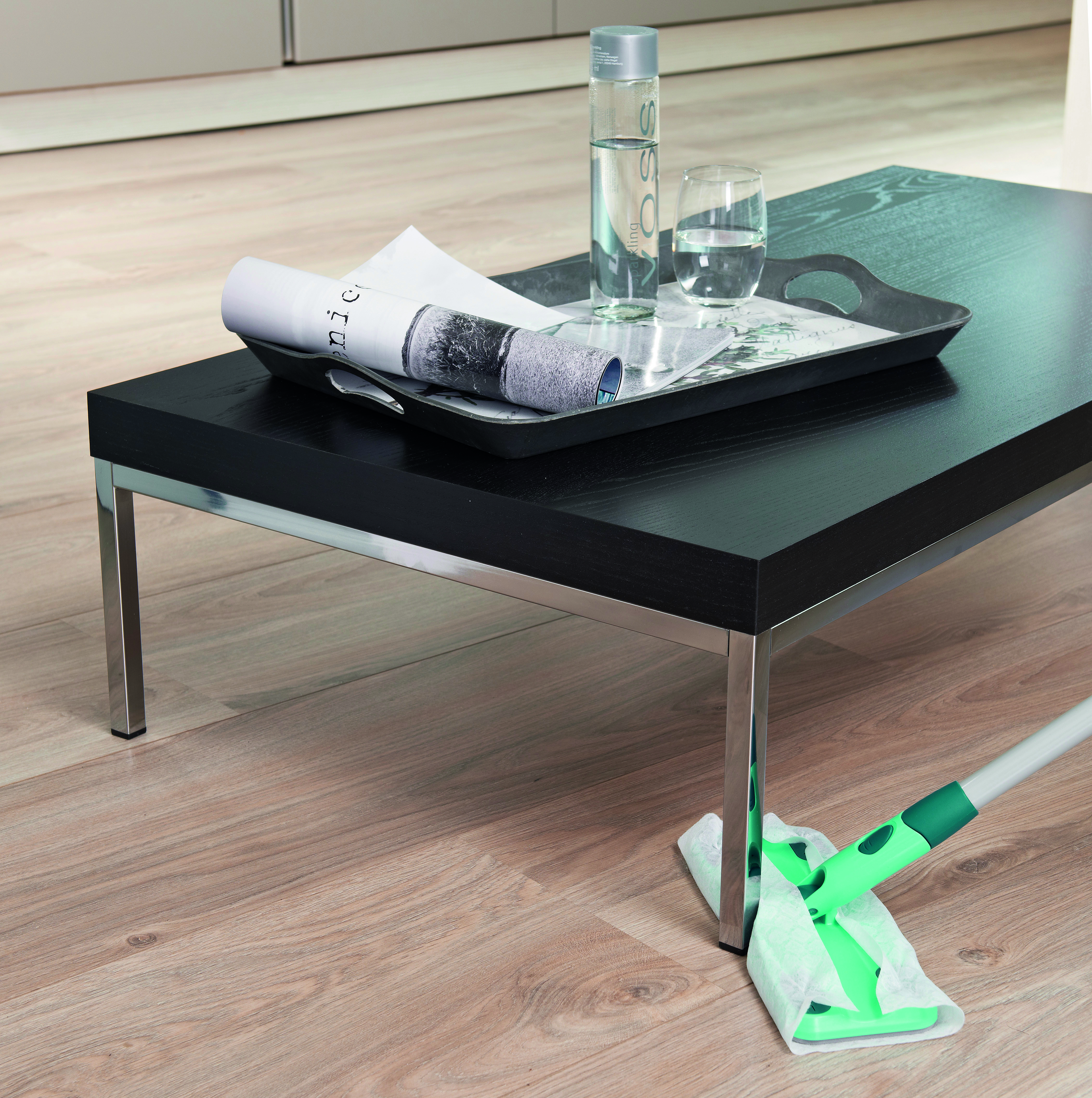 Ein schwarzer Tisch mit Tablett, Flasche, Glas und gerolltem Papier und ein Boden wird gewischt.