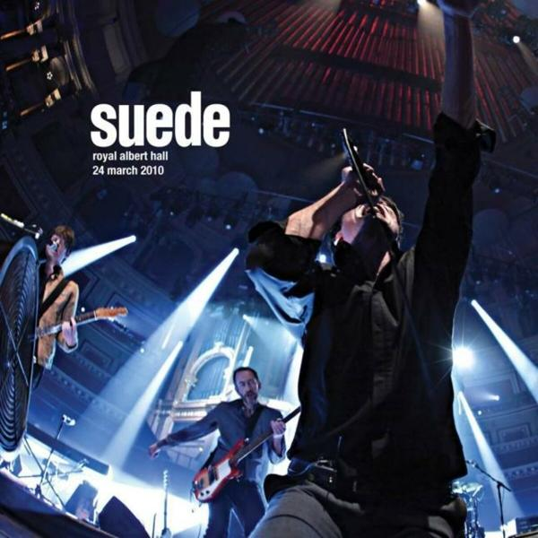 Groupe sur scène. Chanteur avec micro, guitaristes, batterie. Nom du groupe Suede.