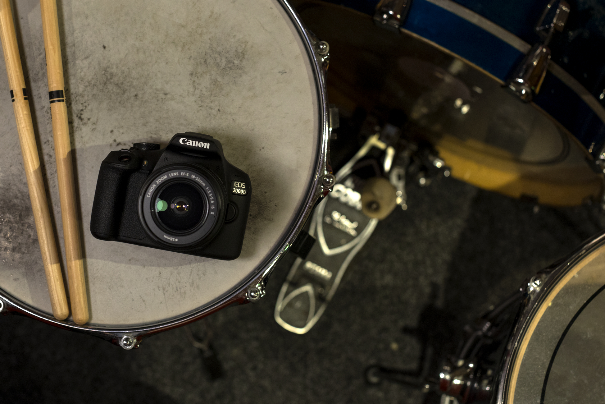 Eine Canon EOS 2000D Kamera auf einer Trommel. Schlagzeugstöcke links.