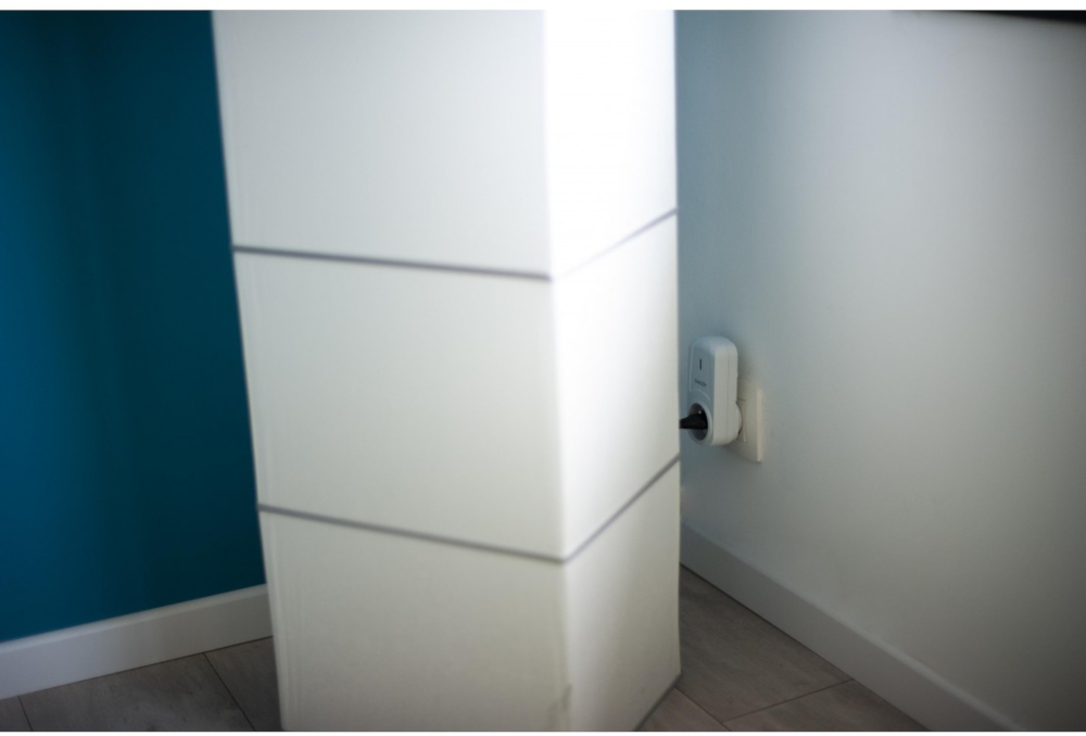 Witte pilaar met grijze lijnen, turquoise muur en stopcontact met oplader.