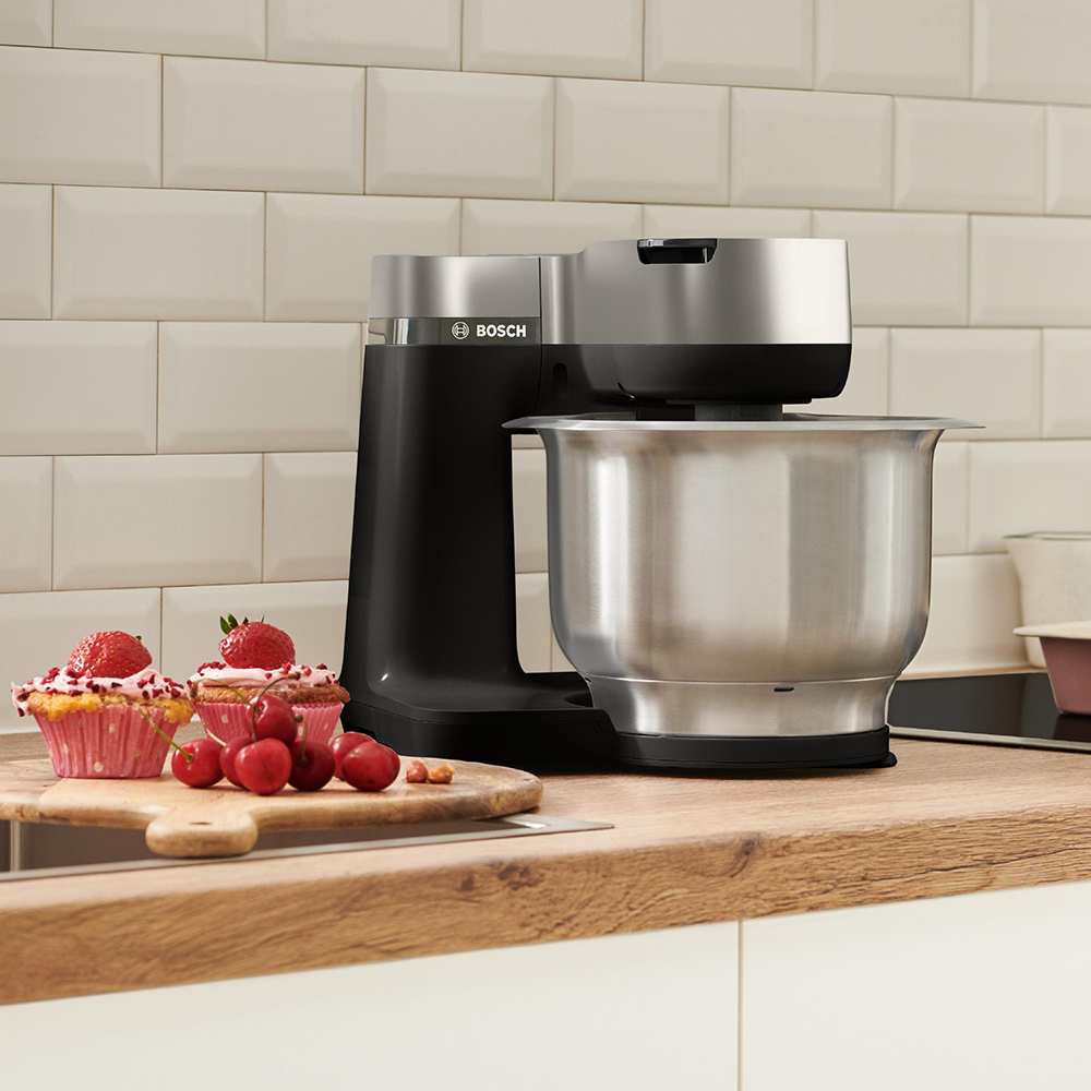 Een keuken met een zwarte en zilveren Bosch keukenmixer, cupcakes en kersen.