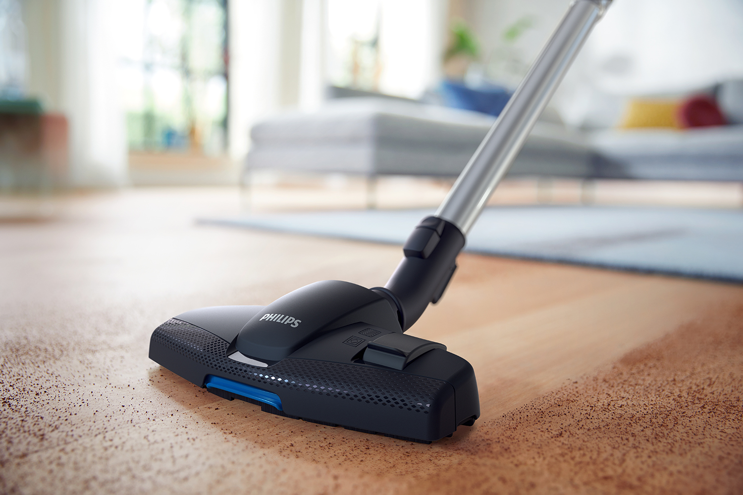 Een zwarte Philips stofzuigerkop op een houten vloer. De achtergrond is wazig, toont een kamer.