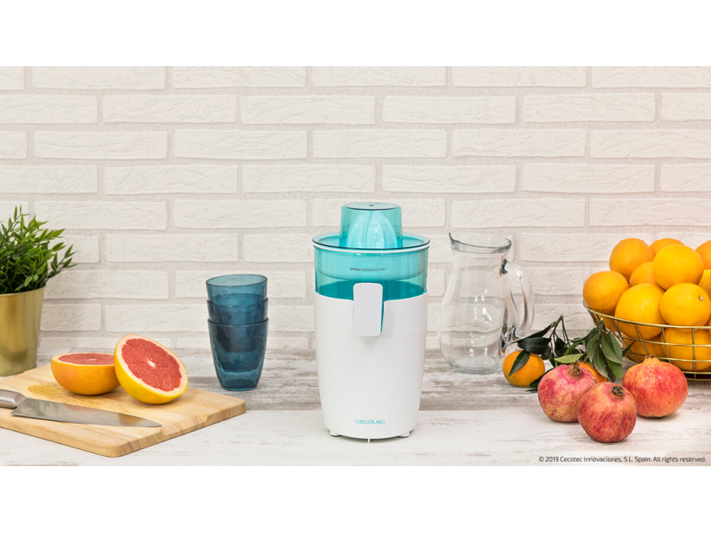 Exprimidor en mesa con fruta, vasos y pared de ladrillos. Colores blanco y azul.