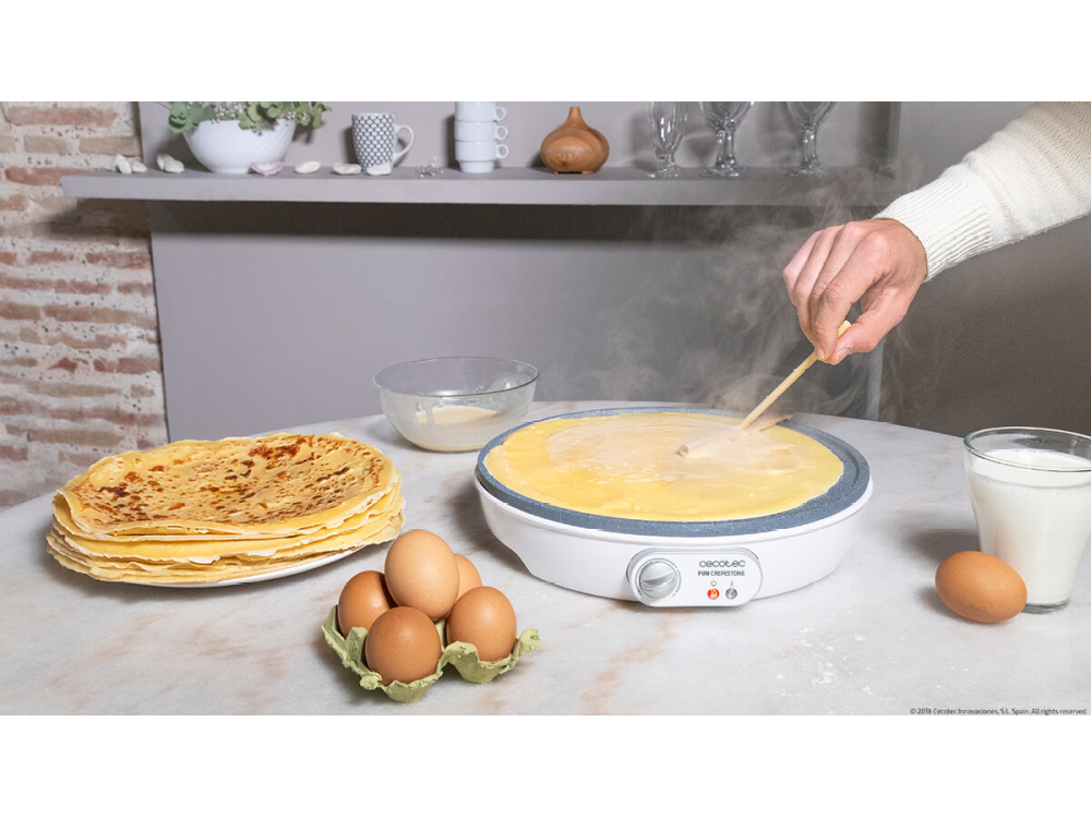 Una persona haciendo crepes. Los ingredientes incluyen huevos, leche y una crepera. Crepes apilados a la izquierda.