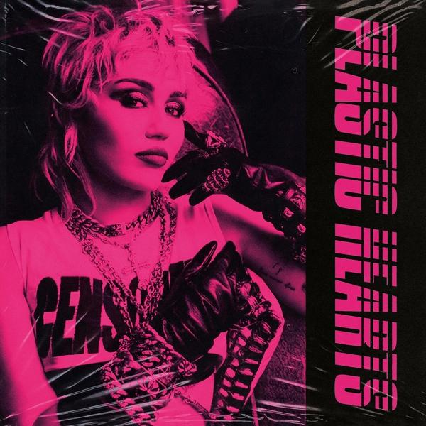 Pochette de l'album de Miley Cyrus. Fond rose, chanteuse en gants noirs et haut. Texte: PLASTIC HEARTS.