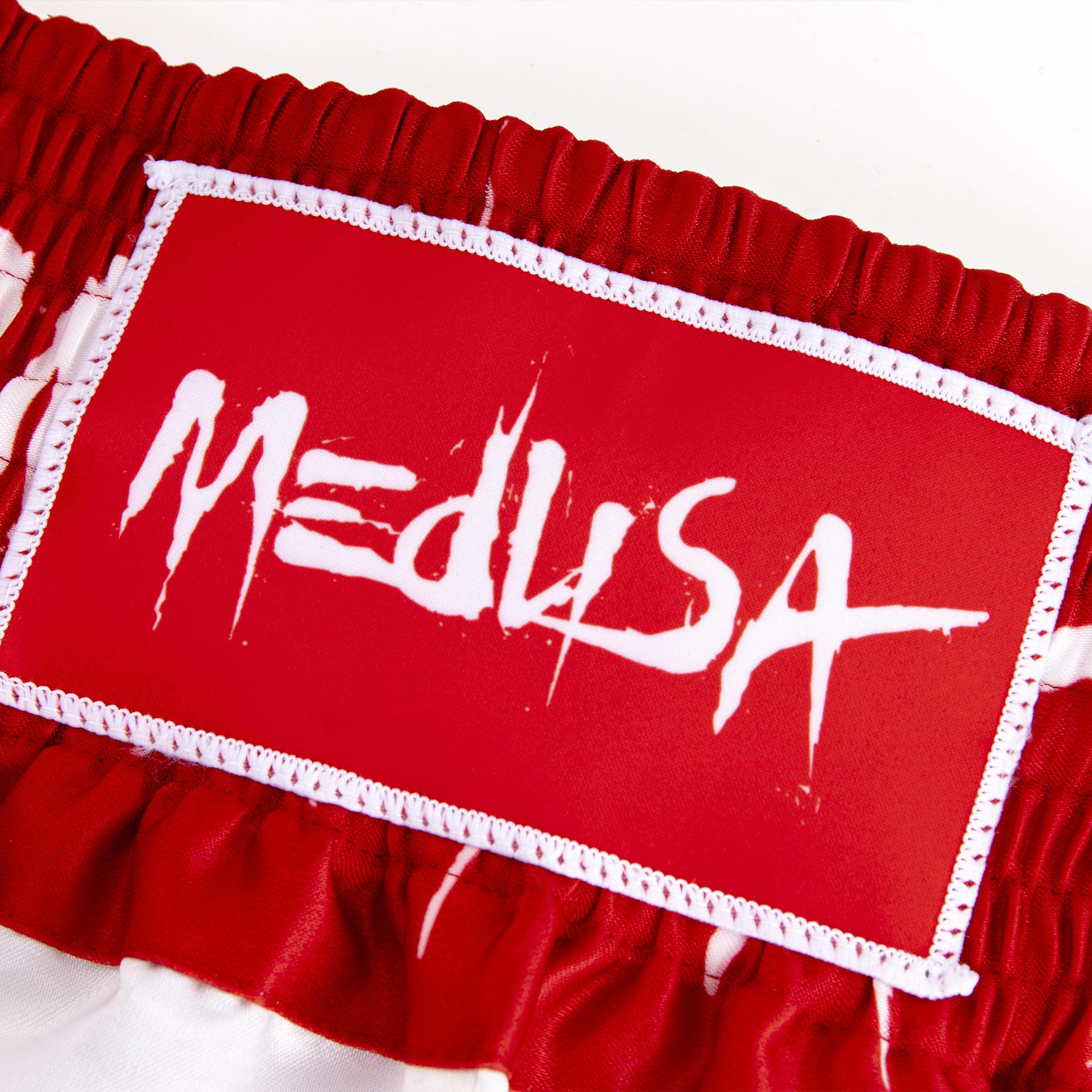 Nahaufnahme des Medusa-Logos in Weiß auf roten Shorts mit weißem Besatz.