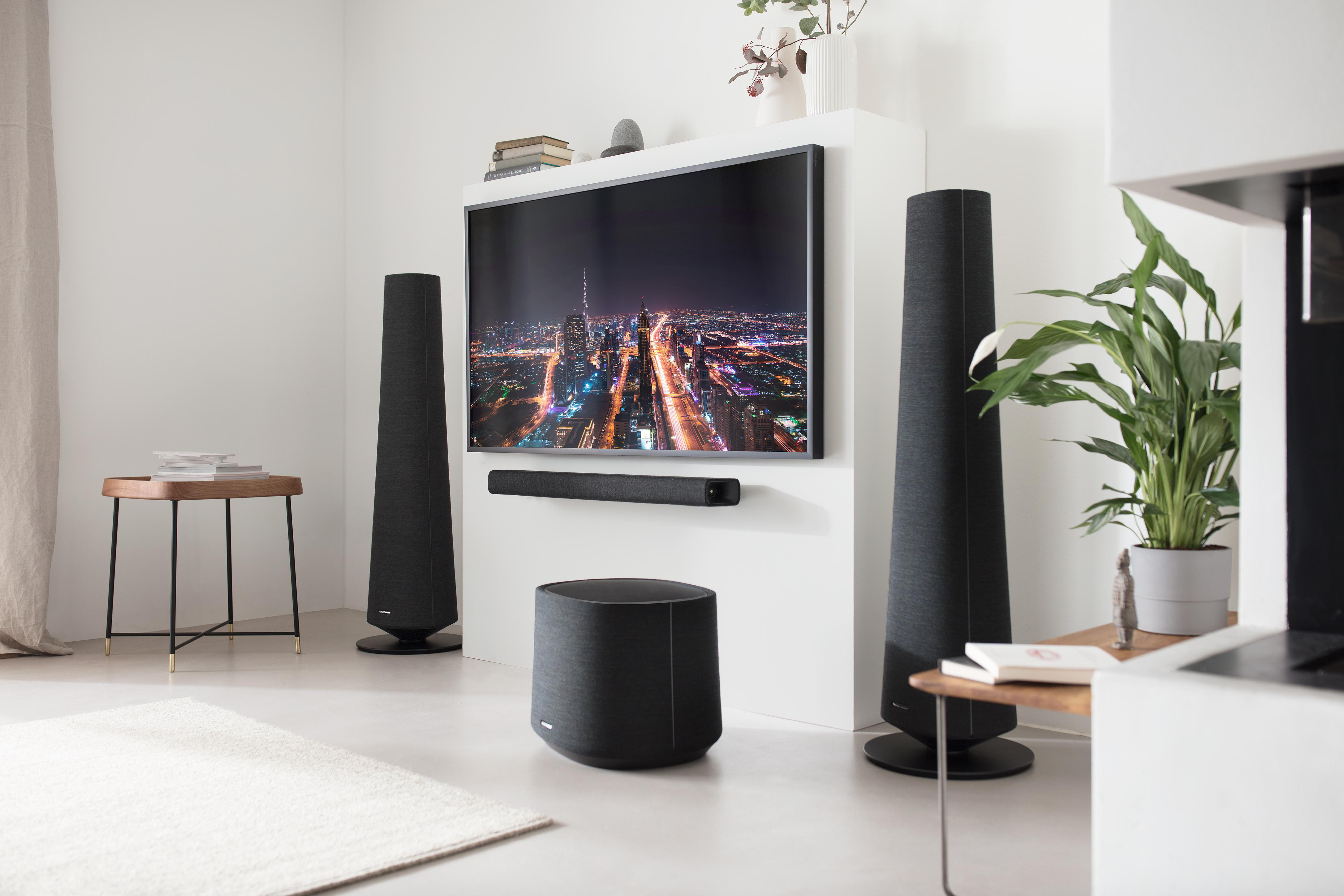 Wohnzimmer mit Fernseher, Soundbar, Lautsprechern und einem Teppich.