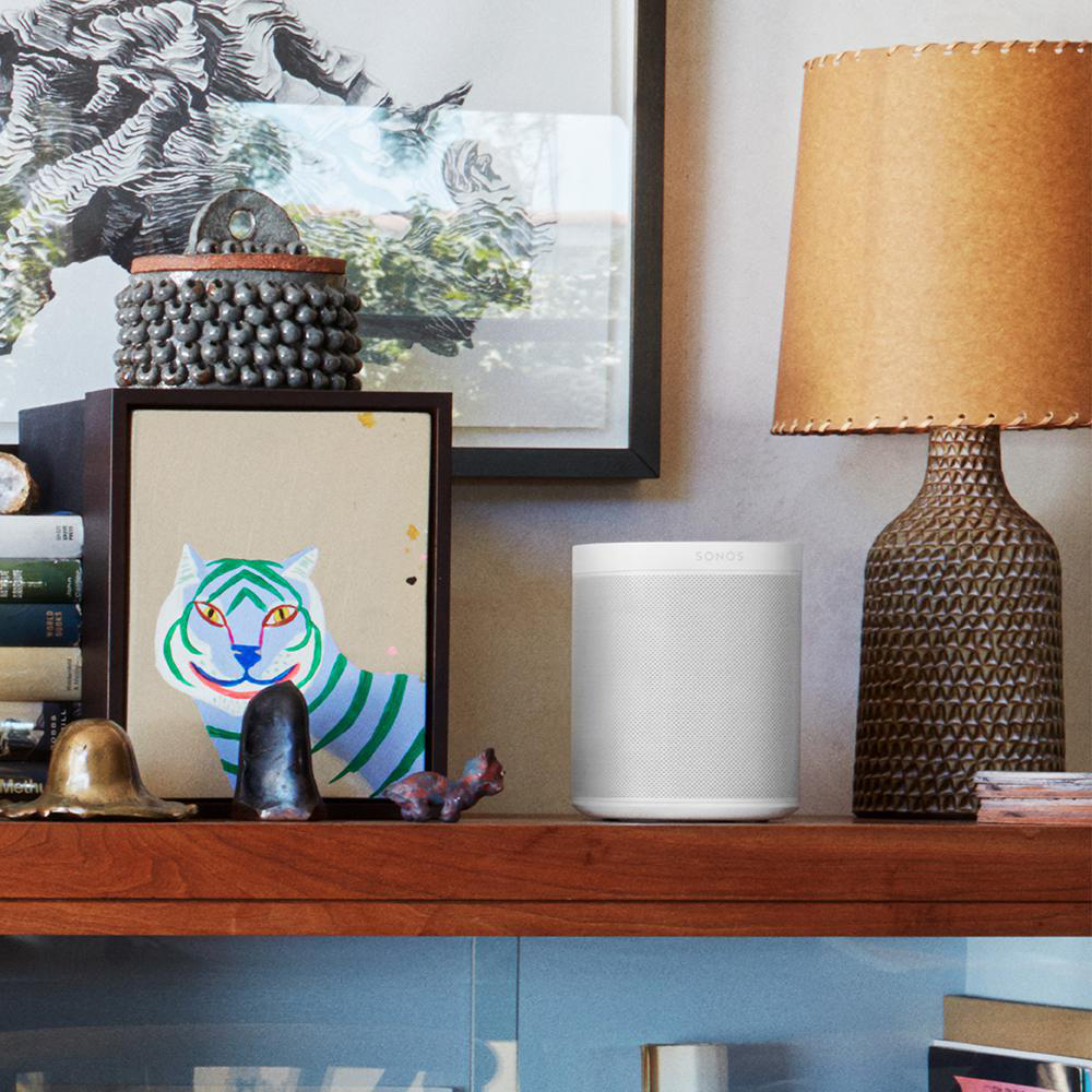 Regal mit Sonos-Lautsprecher, gerahmter Kunst, Lampe, Büchern und dekorativen Objekten. Warme Beleuchtung.