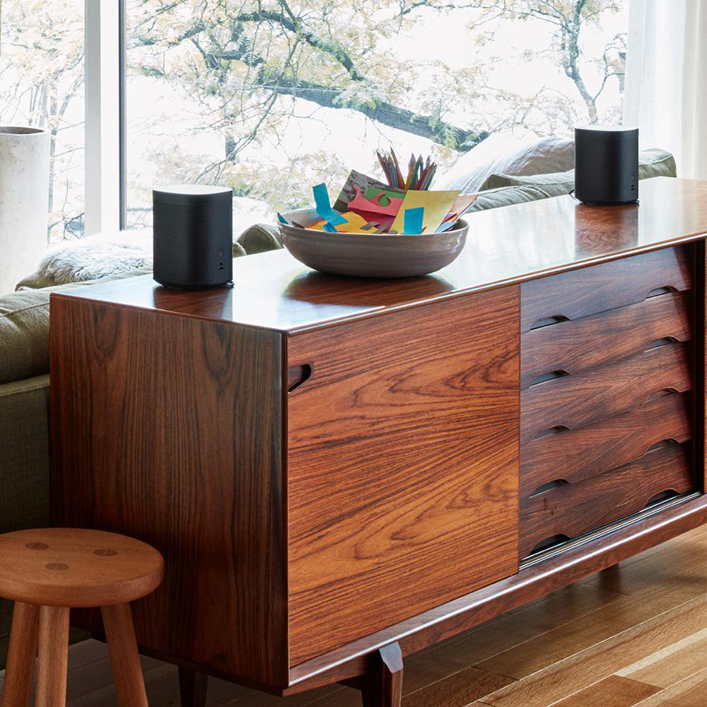 Holzschrank mit Schüssel, zwei Lautsprechern und einem Holzschemel. Im Hintergrund ein Fenster.
