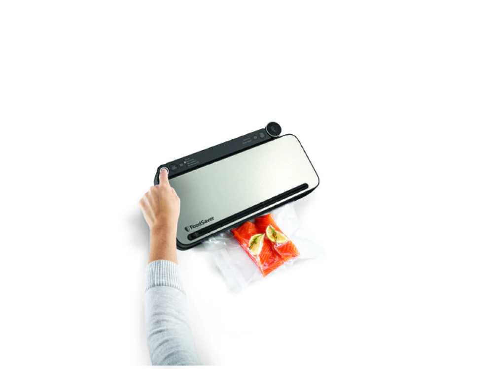 Mano presionando botón en sellador al vacío FoodSaver. Dos filetes de salmón en bolsa.
