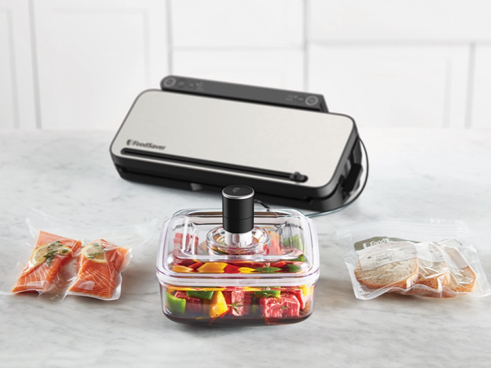 Selladora al vacío FoodSaver con alimentos en bolsas y recipientes: salmón, pimientos y pan.