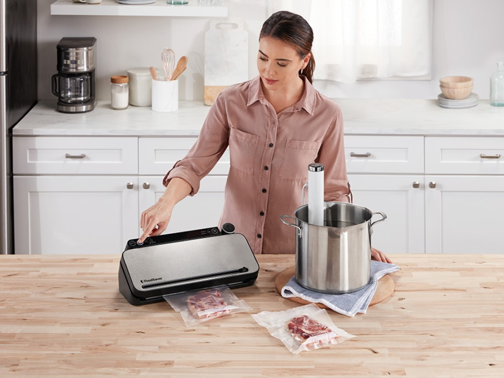 Mujer usando una selladora de alimentos en una cocina. Hay una olla con agua y un dispositivo de sous vide.