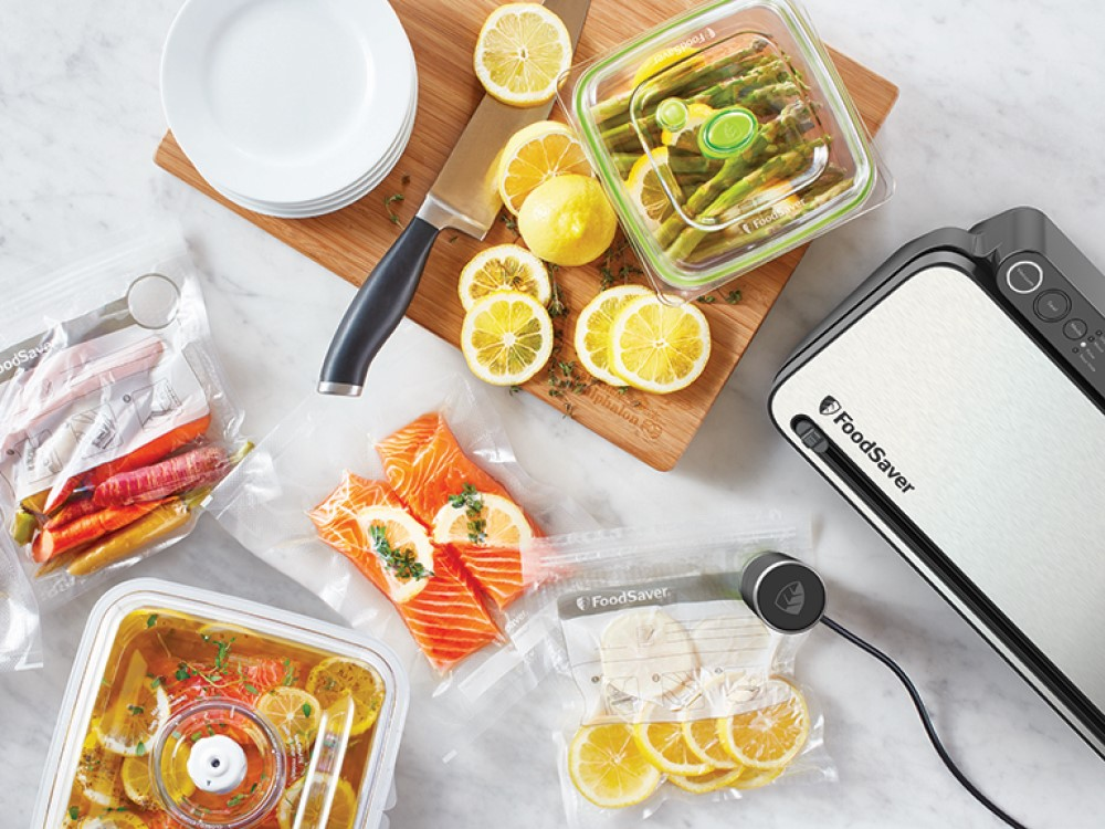 Una envasadora al vacío de alimentos con una tabla de cortar, un cuchillo y alimentos.