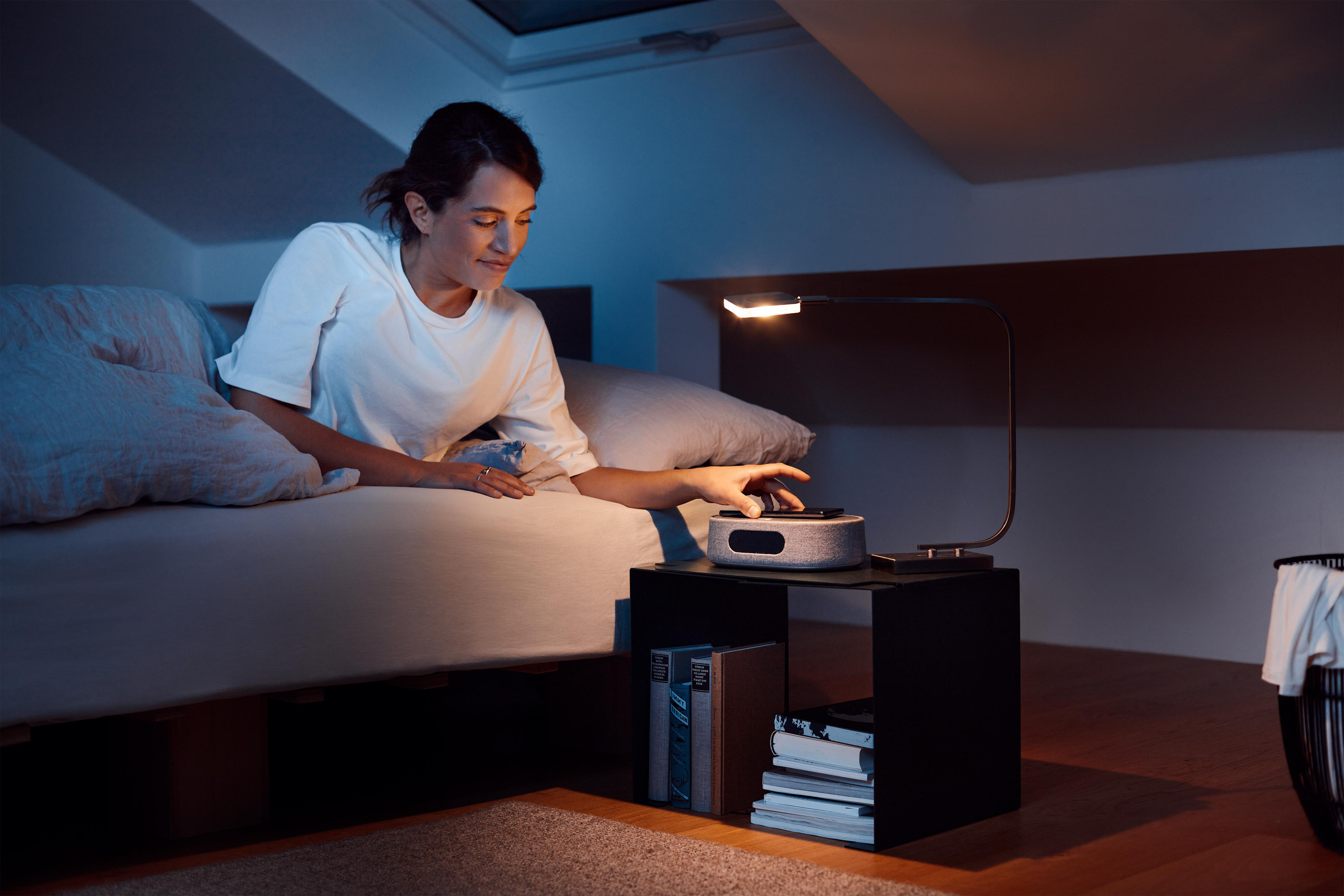 Eine Frau sitzt auf einem Bett und stellt eine Nachttischlampe ein.